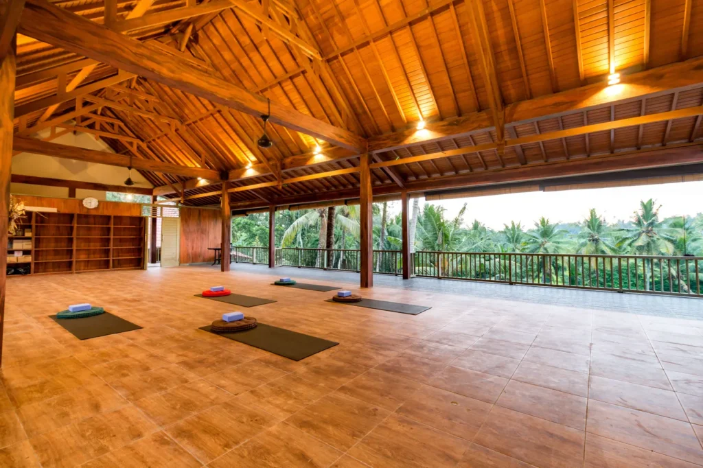 Yoga studio with wooden beams and mats on the floor, open to the landscape, at Umasari Cottage in Ubud