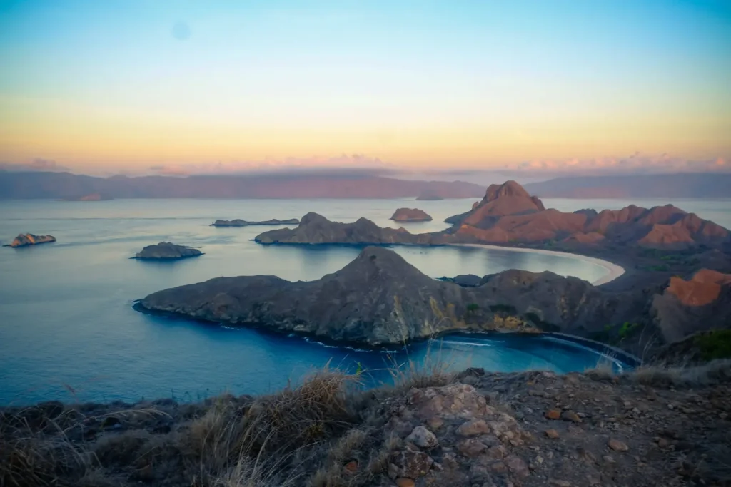 Vue depuis un sommet sur des collines côtières découpées entourant une baie calme au coucher du soleil