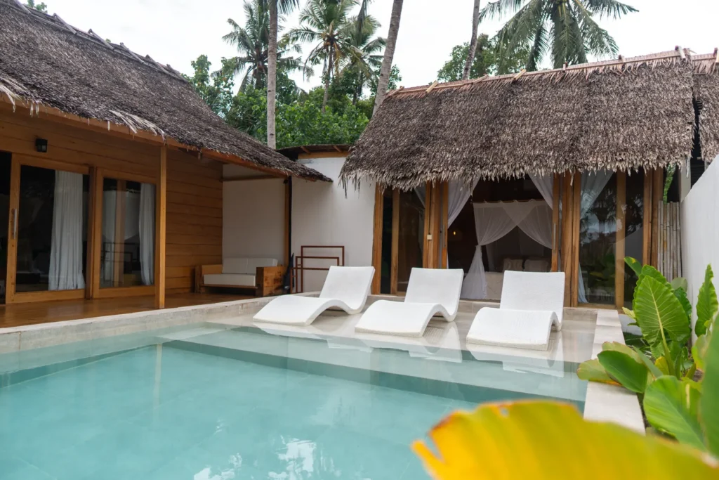 Pool and sunloungers between the thatched buildings of Villa Talara