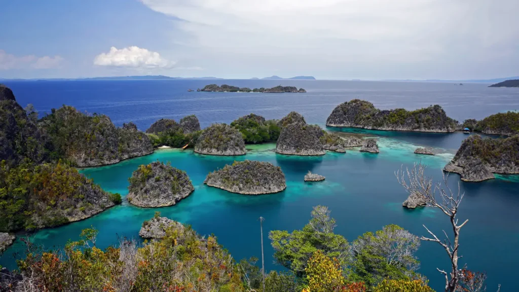 Aerial view of small karst islands covered in green vegetation surrounded by turquoise lagoon water and a deep blue sea
