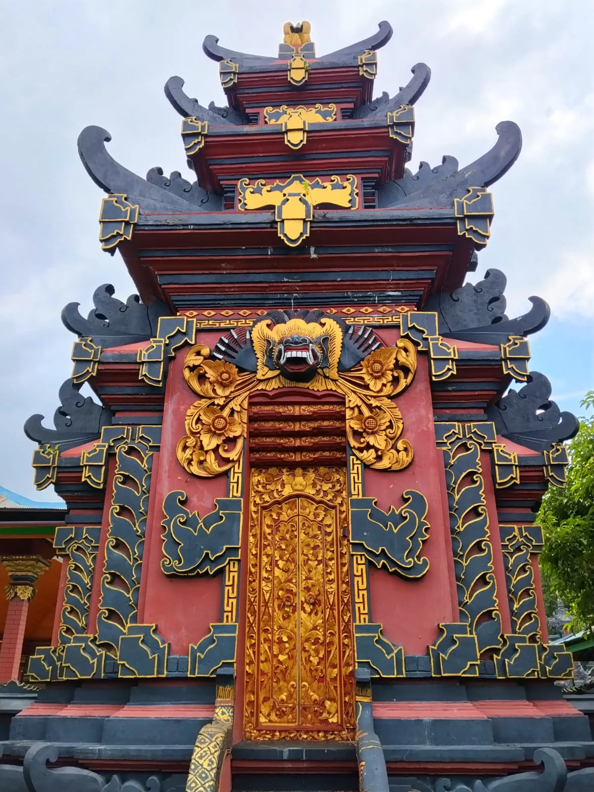 Ornate multi-tiered temple gate with tiered black roof eaves, a fanged golden mask, and a carved gilded door