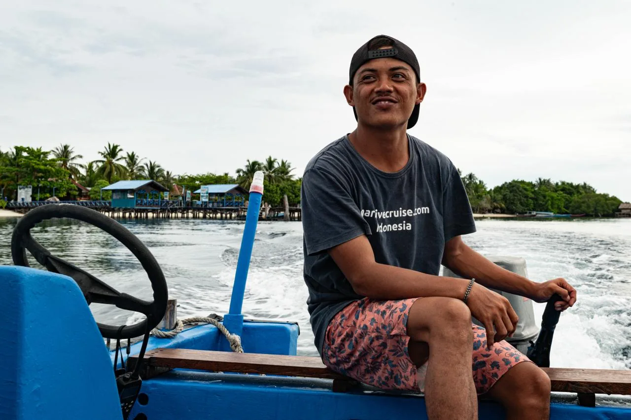 A local boatman steering past a stilt-house village in Raja Ampat