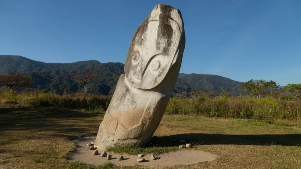 A carved megalithic stone figure standing in the highlands of Sulawesi