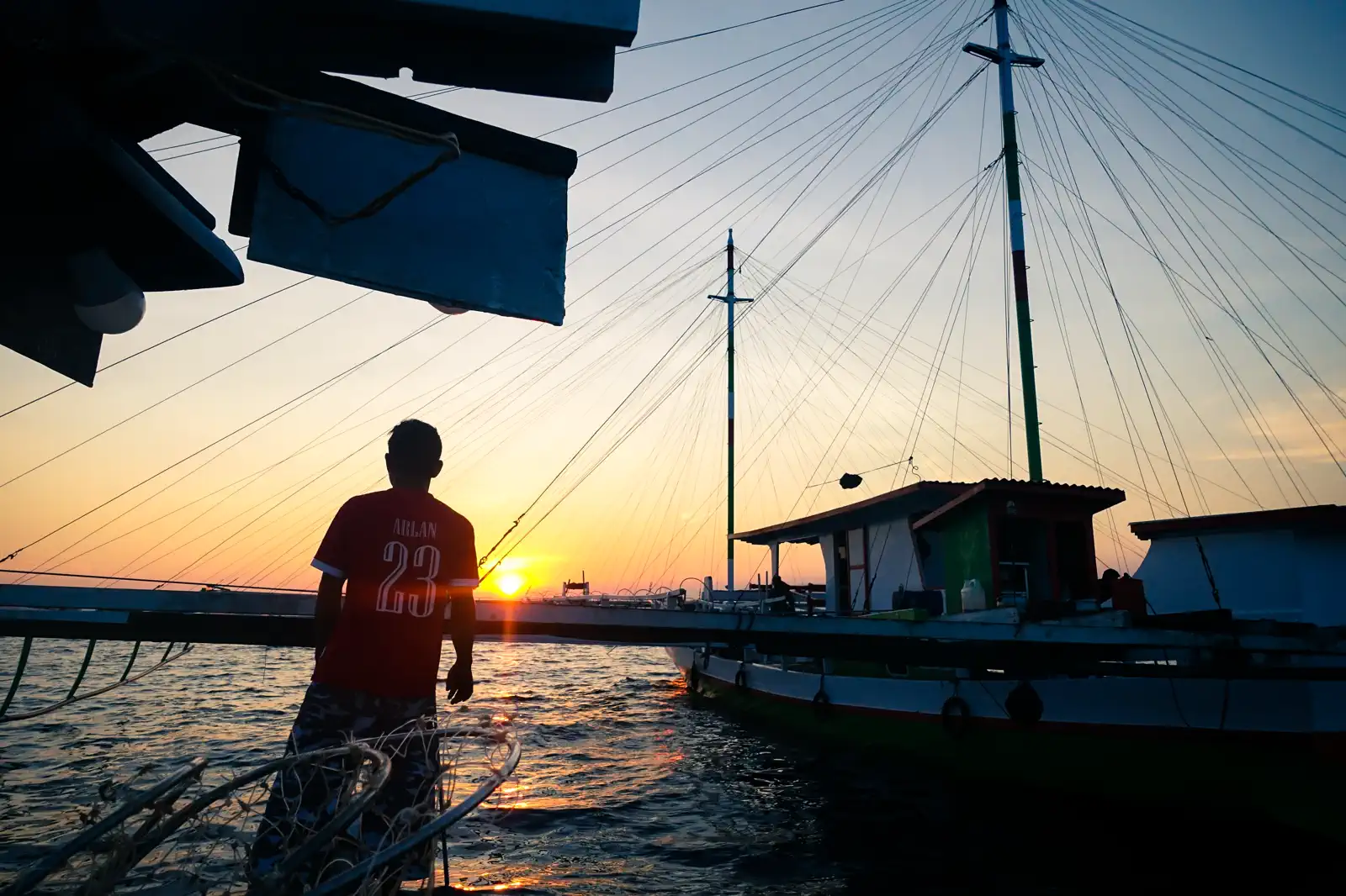 A bagan lift-net platform at sunrise in Saleh Bay, a fisherman standing on the deck beside the net rigging