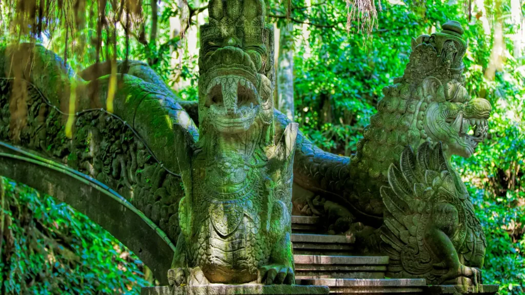 Moss-covered stone naga statues beside a jungle staircase in the Sacred Monkey Forest, Ubud