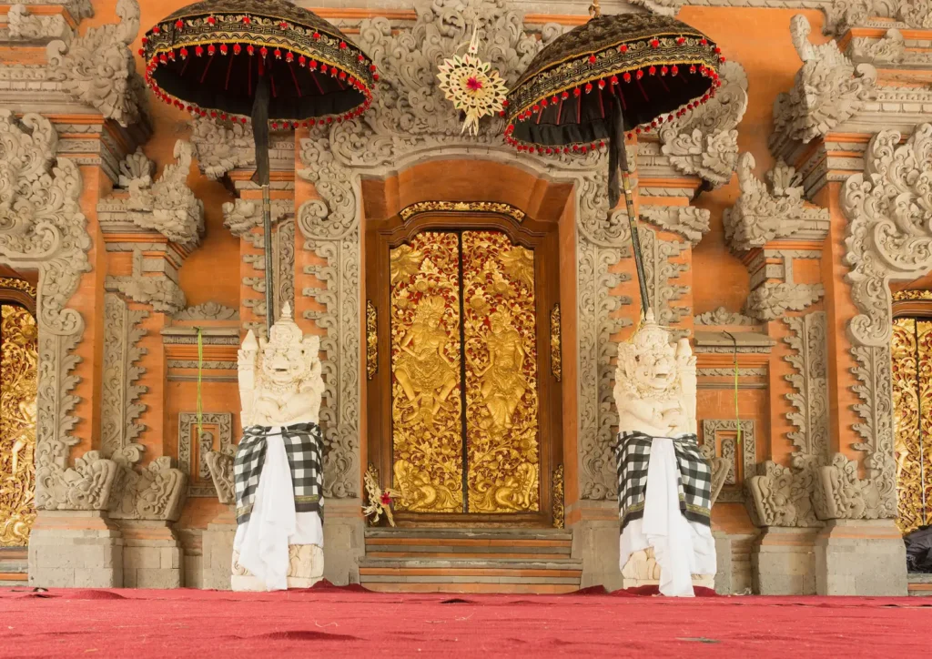Gilded doors and carved red-and-gold gate with guardian statues inside Ubud Palace