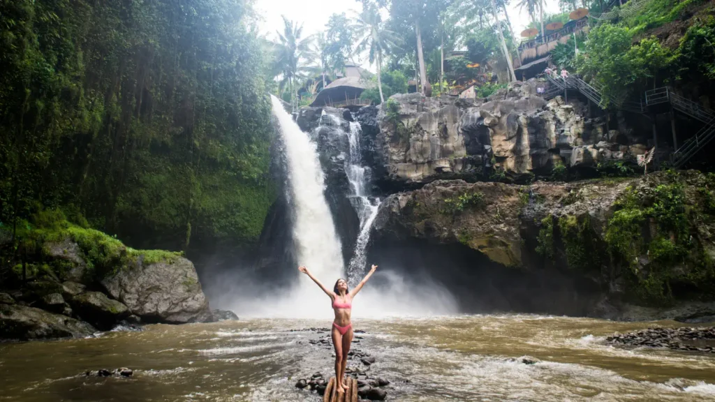 Visitor standing with raised arms below Tegenungan Waterfall