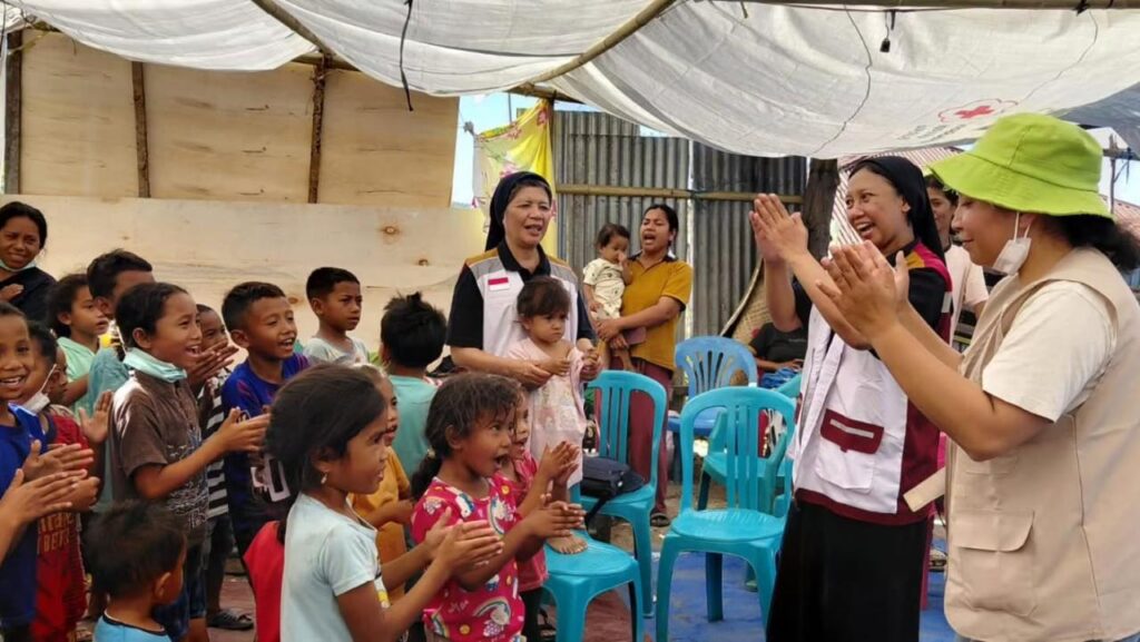 Children and volunteers singing together under a tarpaulin shelter at a camp after the earthquake
