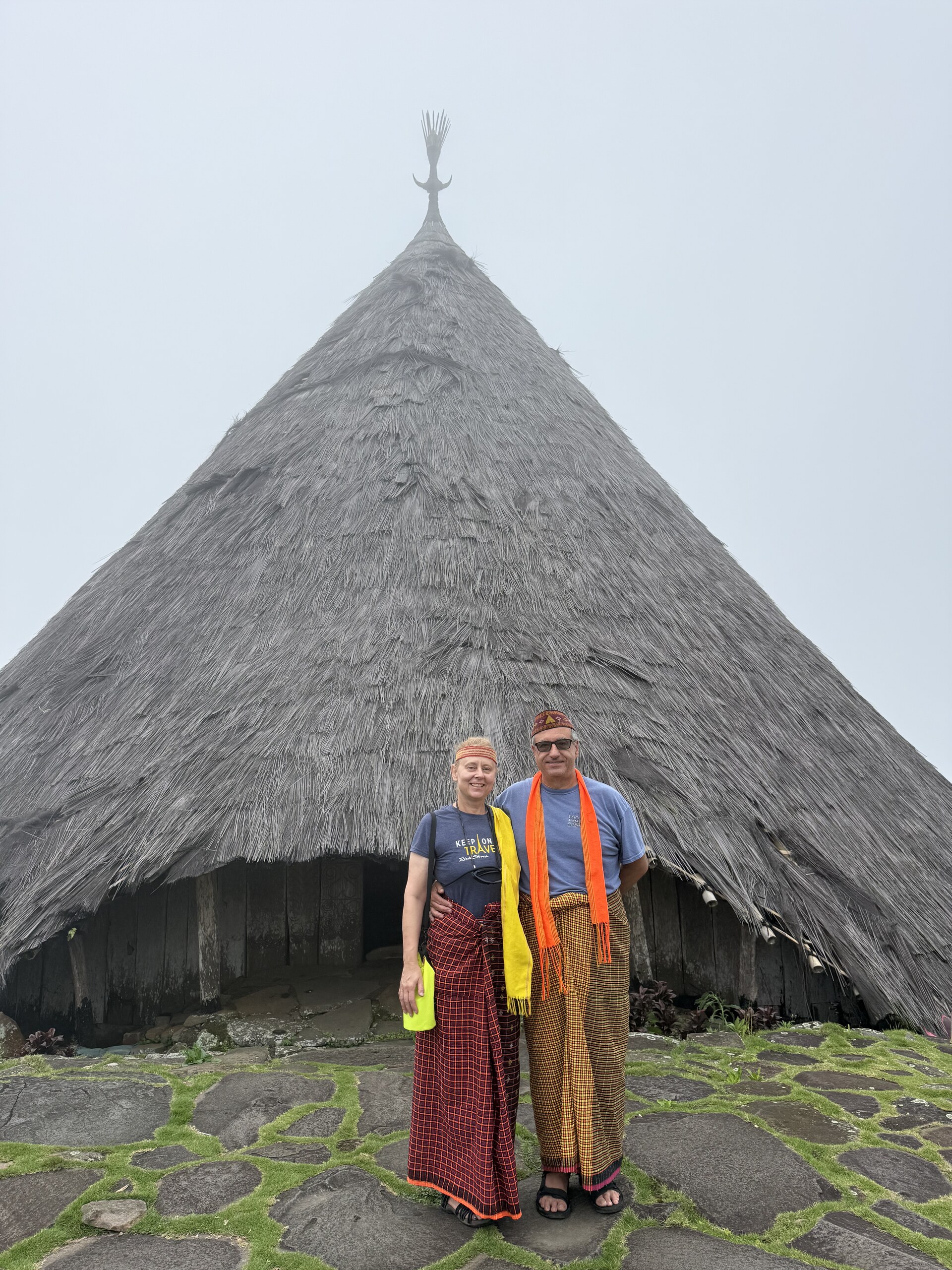 Dean and Zita in Manggarai dress in front of a large conical drum house