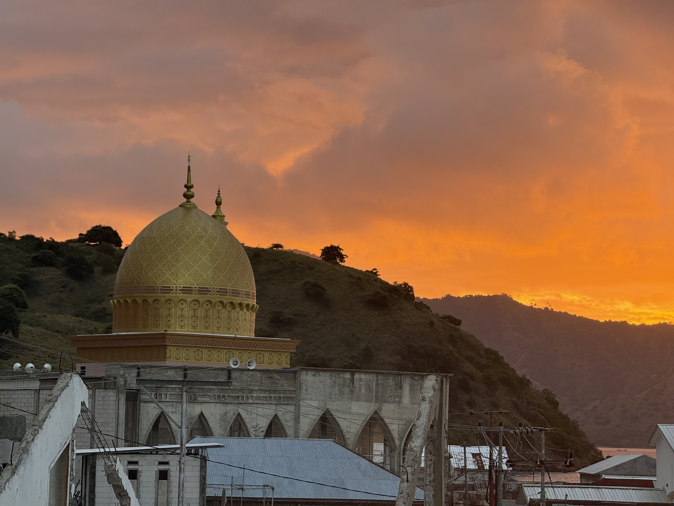 The golden dome of a mosque in Labuan Bajo against an orange sunset sky