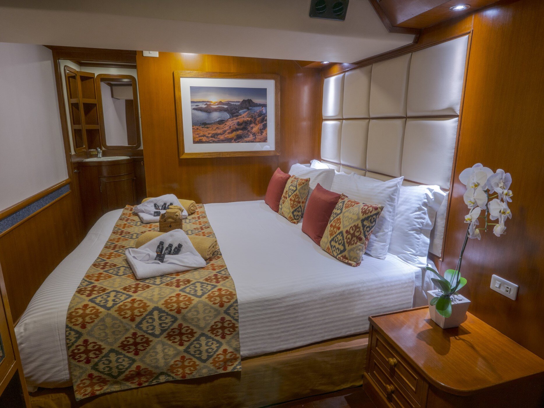 Deluxe cabin on the Mermaid I set up with a double bed, patterned runner and an orchid on the side table