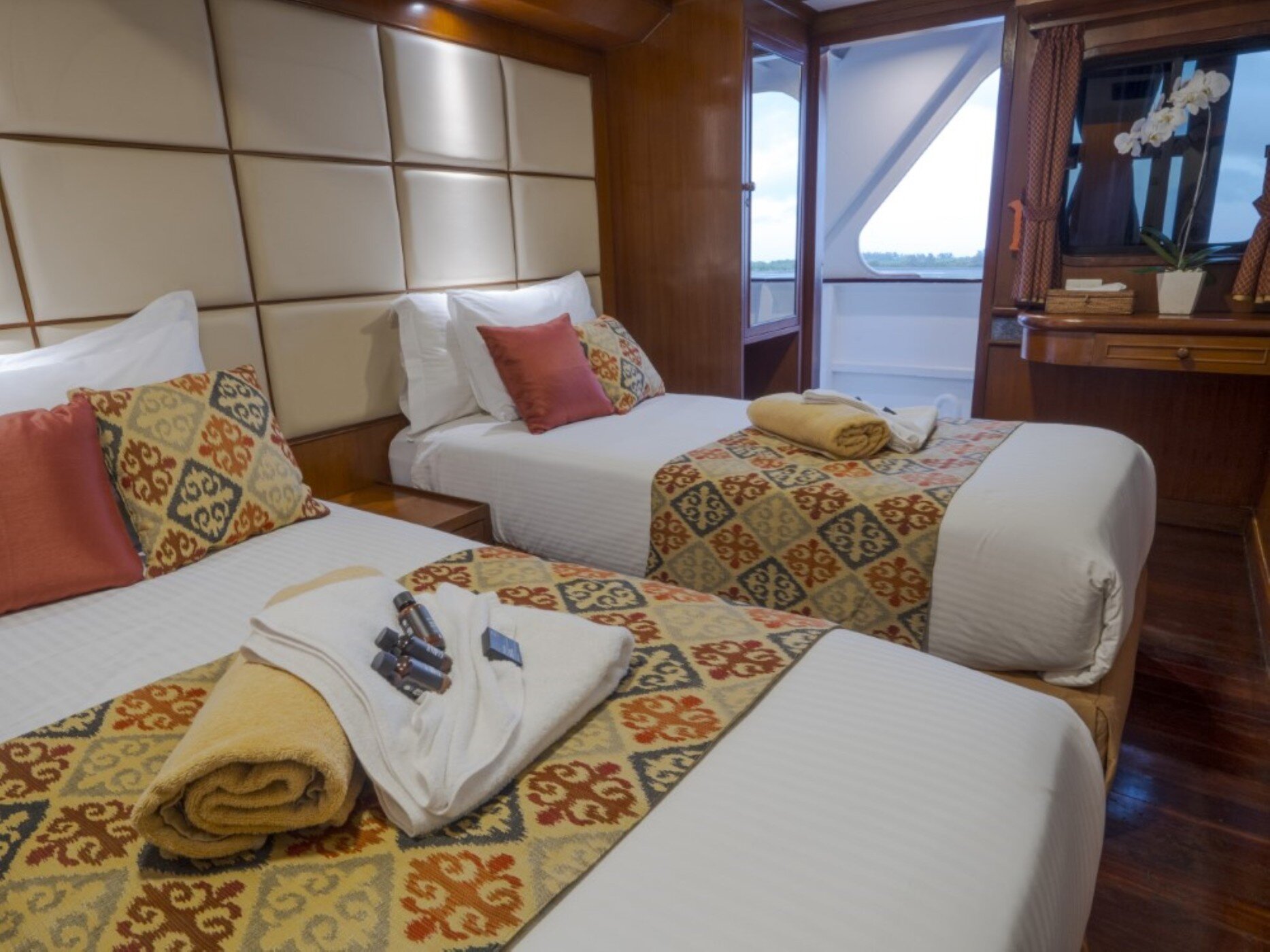Twin bed deluxe cabin on the Mermaid I with towels folded on the bed and a writing desk