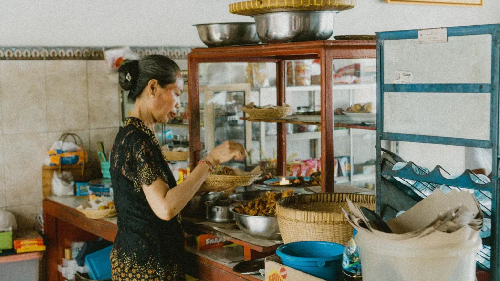 Woman serving nasi campur at the counter of Warung Teges