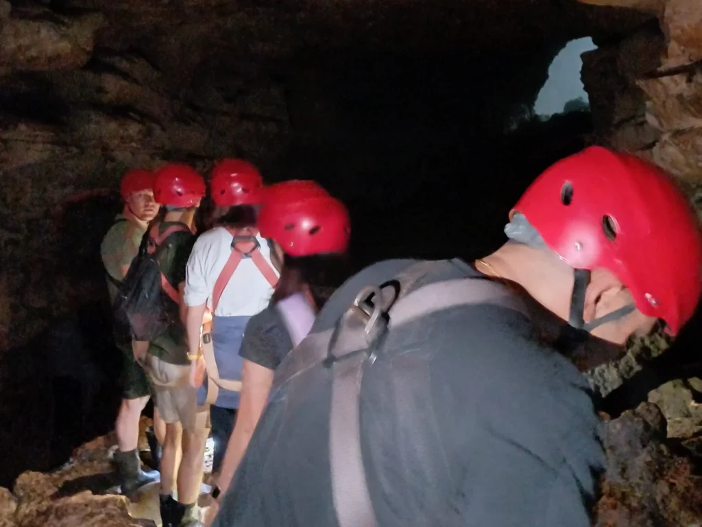 Visitors in red helmets walking through the tunnel at Jomblang Cave