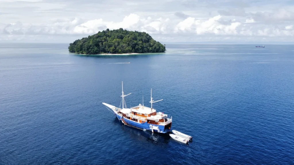 Aerial view of the phinisi Kurabesi Nusantara at anchor off a small forested island