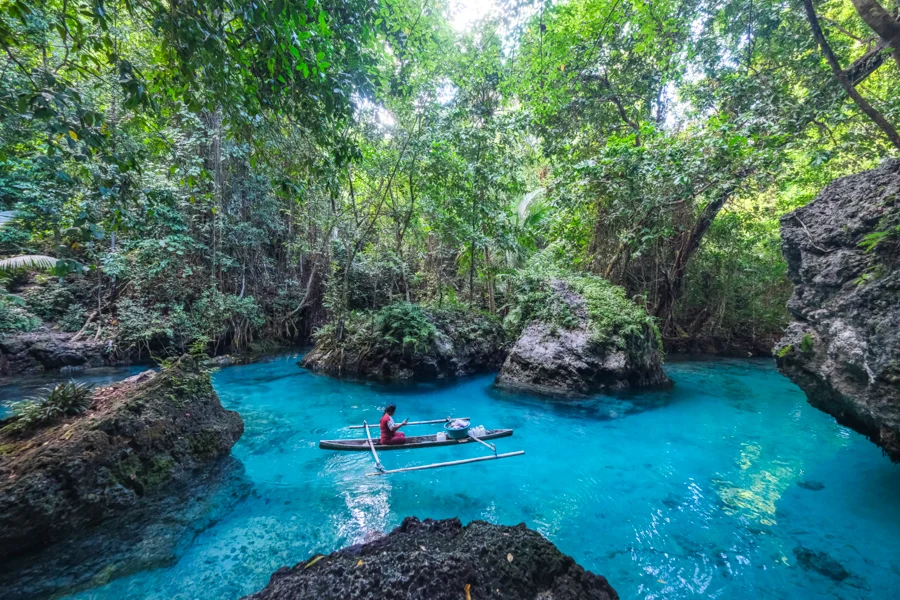 Outrigger canoe in the turquoise spring pool at Paisu Batango on Peleng, between grey limestone boulders