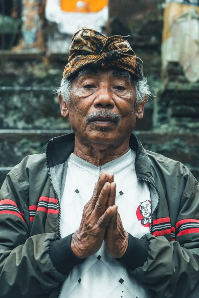 Balinese elder in an udeng headcloth with his hands pressed together in prayer at a temple