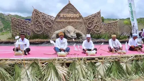 Elders in white seated before a dragon carving at a traditional ceremony on Komodo Island