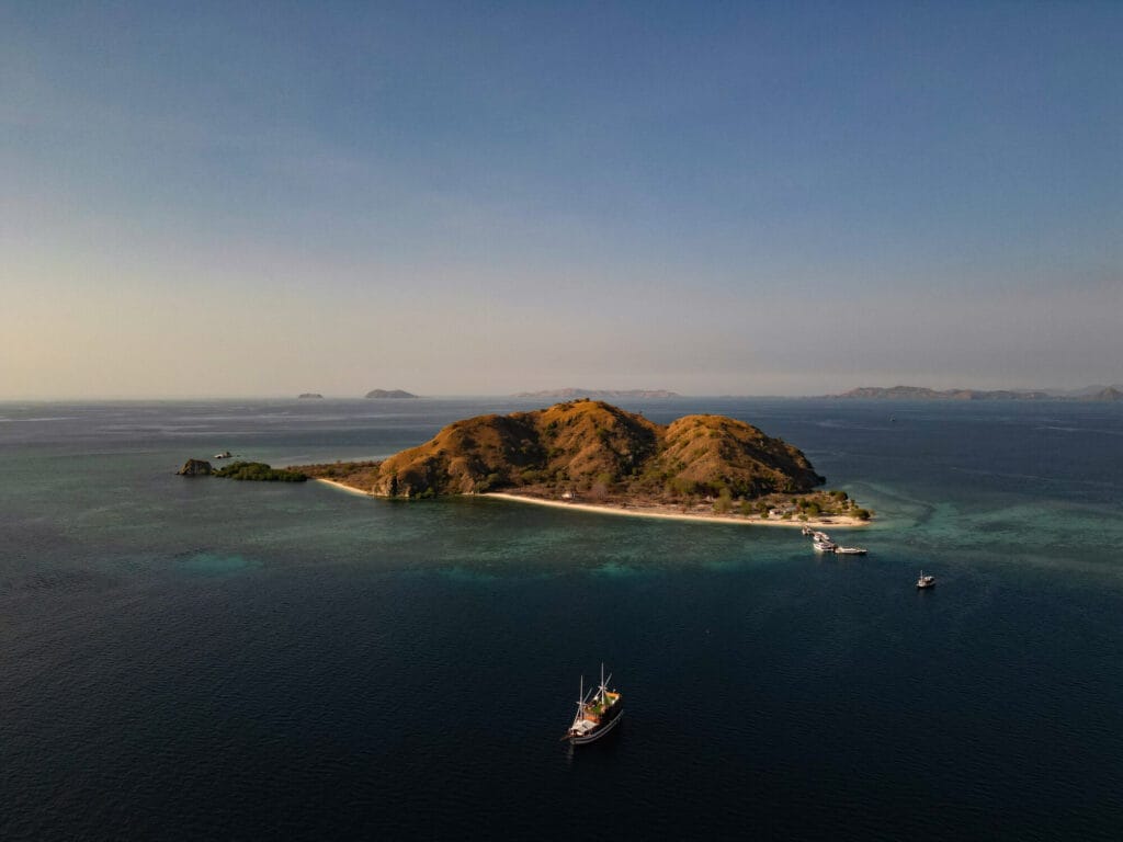 Aerial view of an island in Komodo National Park, with a phinisi at anchor