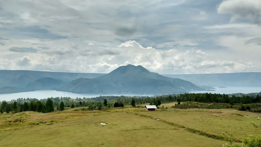 Grassland above Lake Toba, with a volcanic hill across the water under low cloud