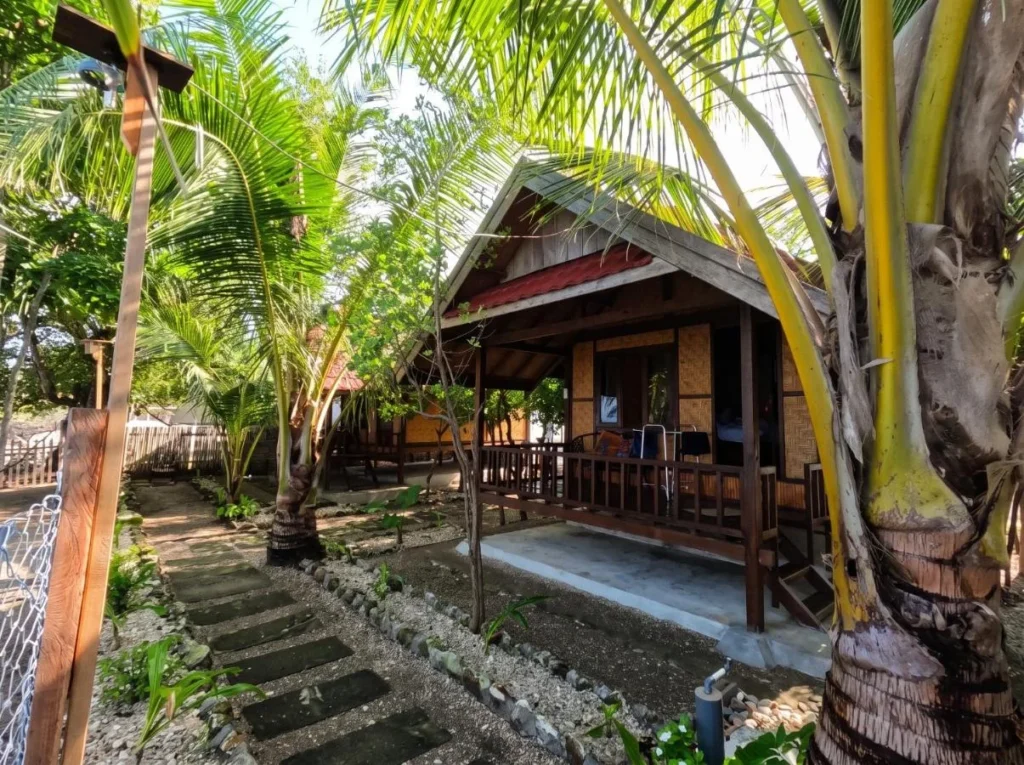 A wooden bungalow with a thatched roof and a front porch among palm trees at Maryan Moyo, Moyo Island