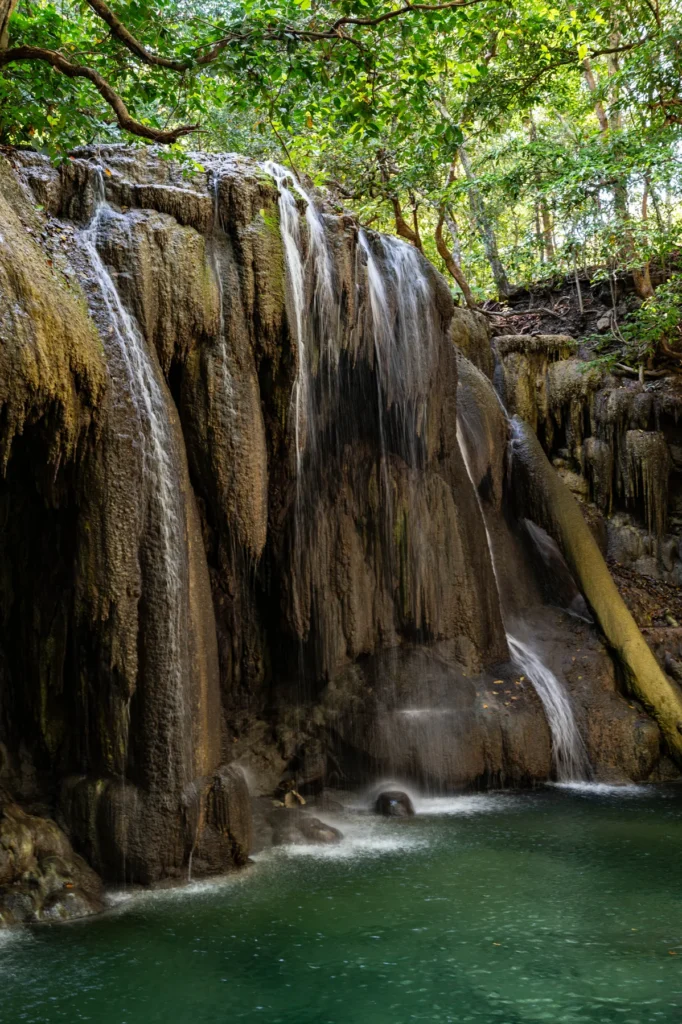 Mata Jitu waterfall on Moyo Island, pouring over mossy limestone into a green pool in the forest