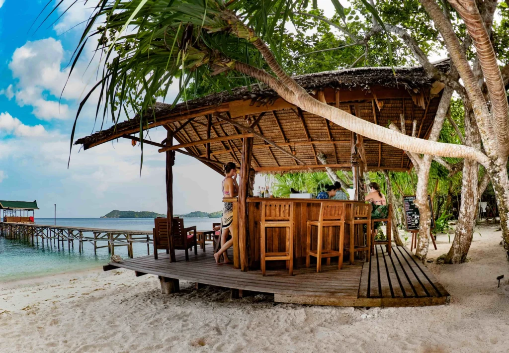 Beach bar with a thatched roof on the white sand, jetty behind