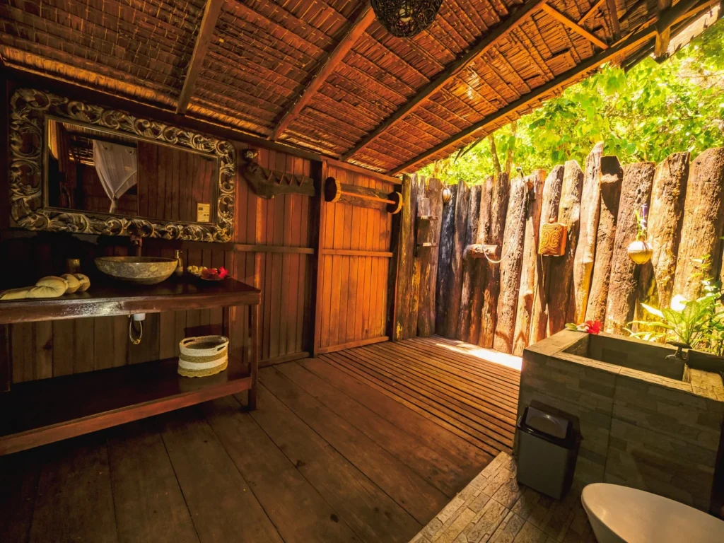Semi-open bathroom of a Deluxe Cottage with wooden walls and plants