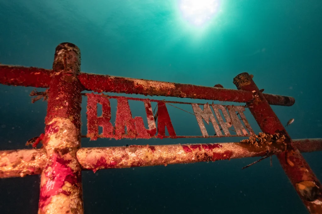 The Raja Ampat sign underwater, a red frame under green, sunlit water
