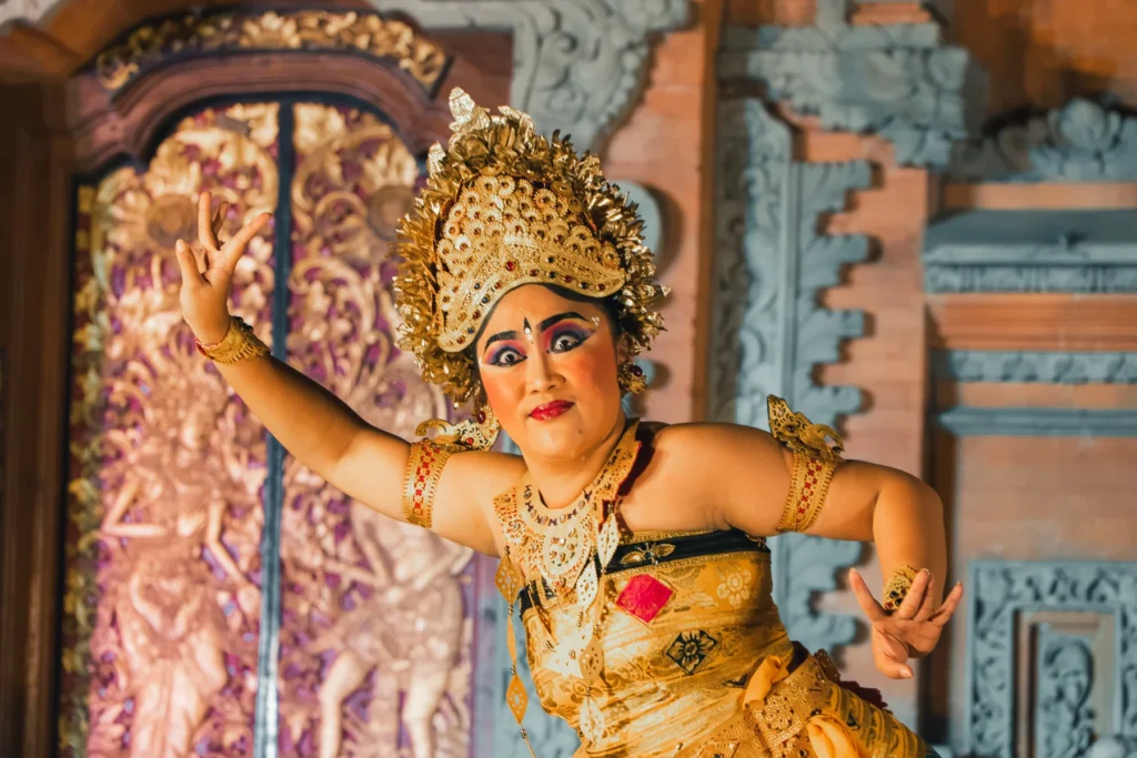 Legong dancer in a gold costume and headdress performing on the carved stage at Ubud Palace
