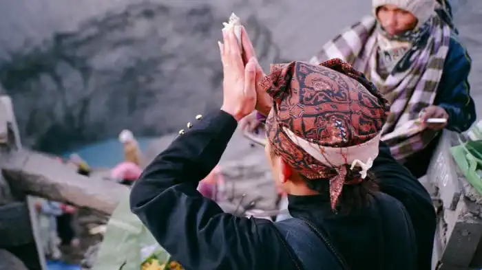 A Tengger man in a batik headcloth prays with raised hands at the rim of Bromo's crater